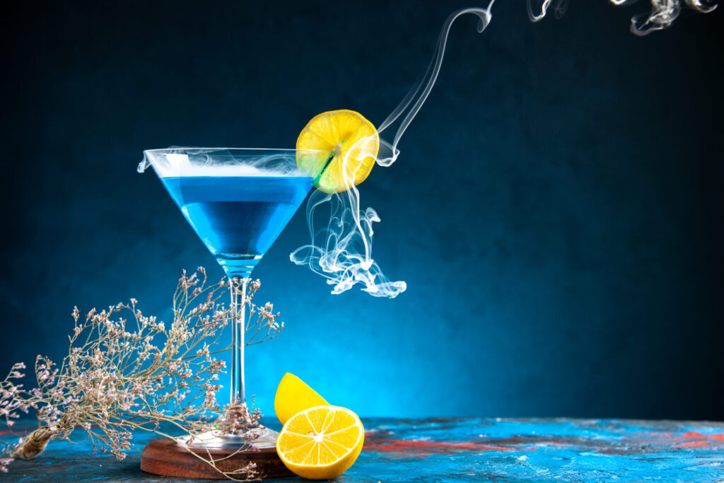 top-view-alchocol-cocktail-glass-goblet-served-with-lemon-slice-fir-branches-right-side-blue-table